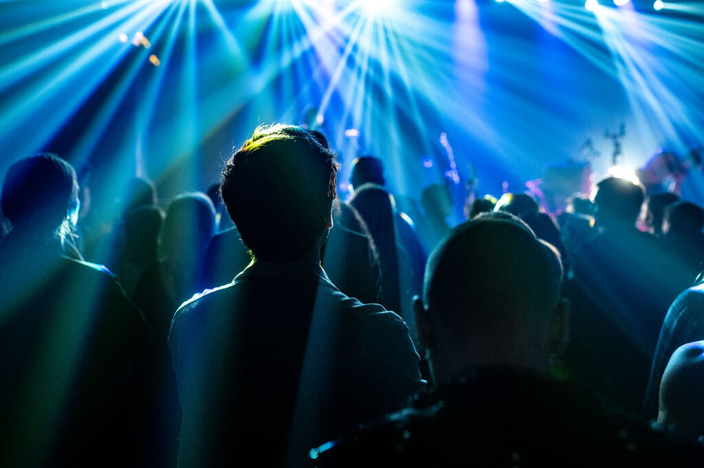 Publiczność w klubie, oświetlona mocnymi, niebieskimi promieniami scenicznymi, widok na Atmosferę Folkowe Ucho Dziady.